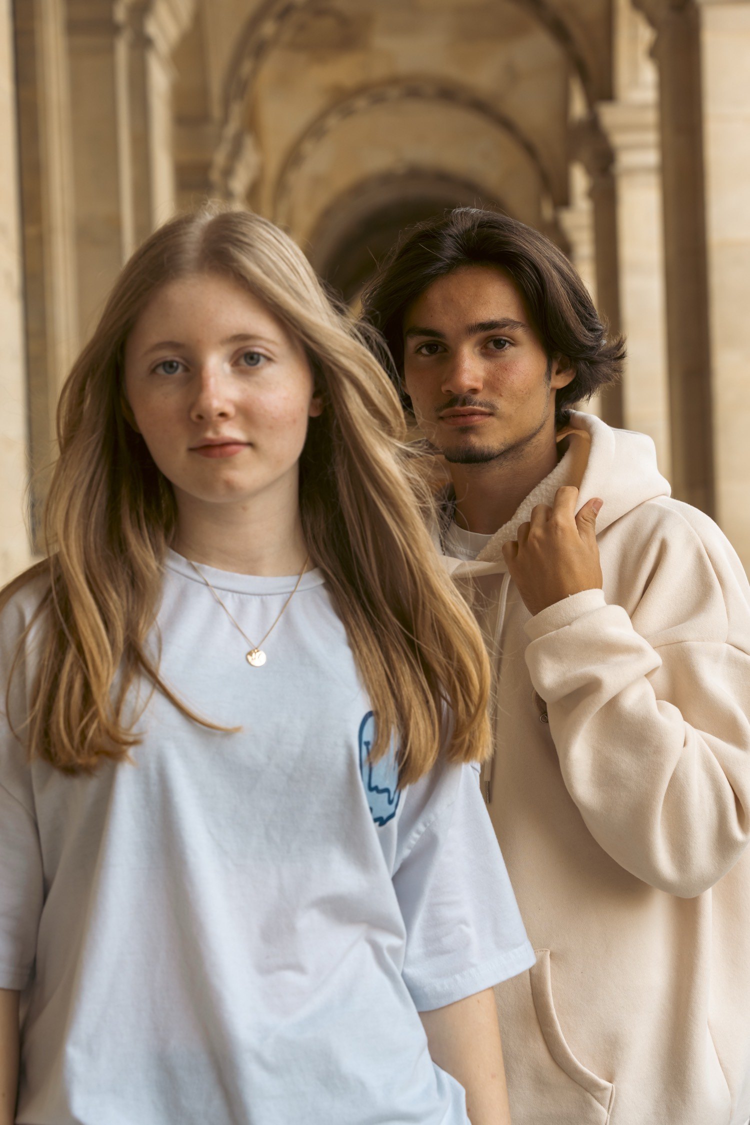 Jeune femme et jeune homme dans une galerie à arcades, t-shirt et hoodie clairs