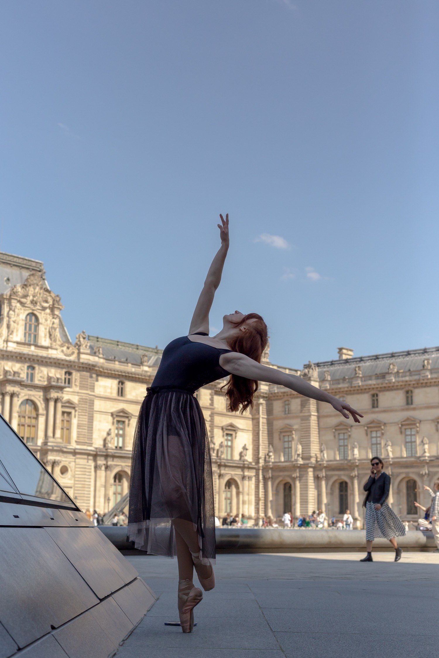 Danseuse en tutu devant le Louvre, arabesque en équilibre, ciel bleu
