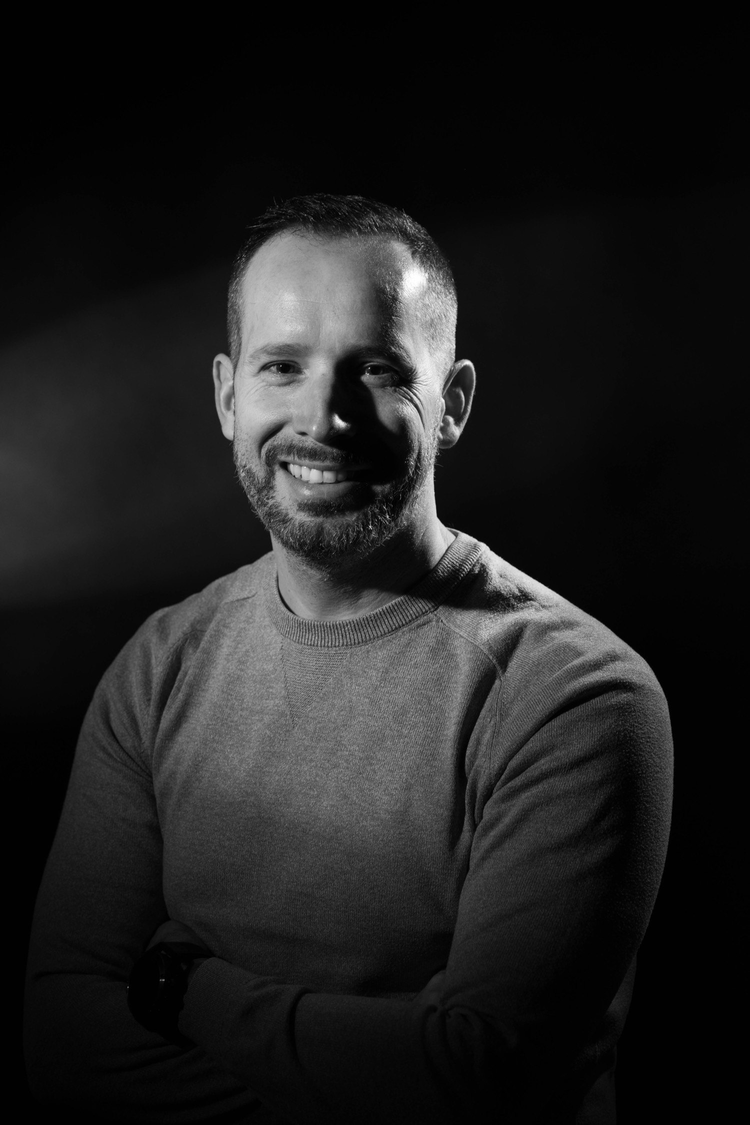 Portrait dramatique en noir et blanc d’un homme souriant, pull, fond noir